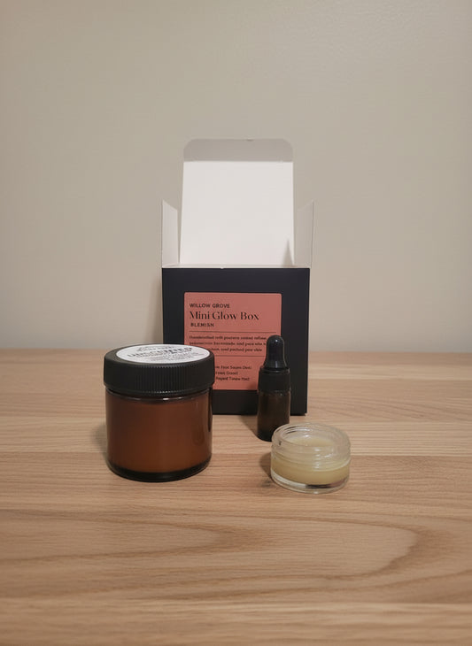 Skincare products including a jar of tallow, mini dropper bottle of serum, and small container of eye cream on a wooden surface with a box in the background.